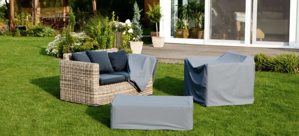 Rattan-Lounge im Garten, Sessel und Hocker mit grauen Schutzhauben
